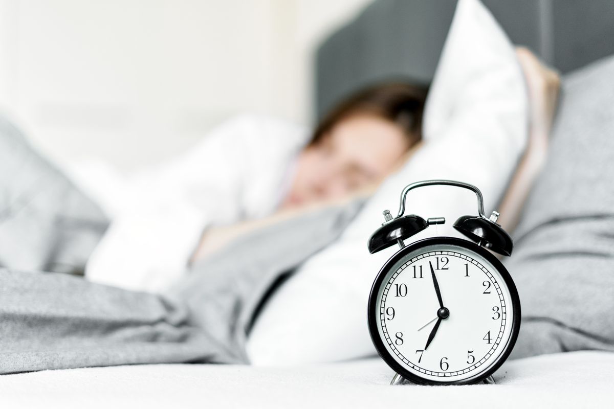 Despertador junto a una cama con una persona descansando.